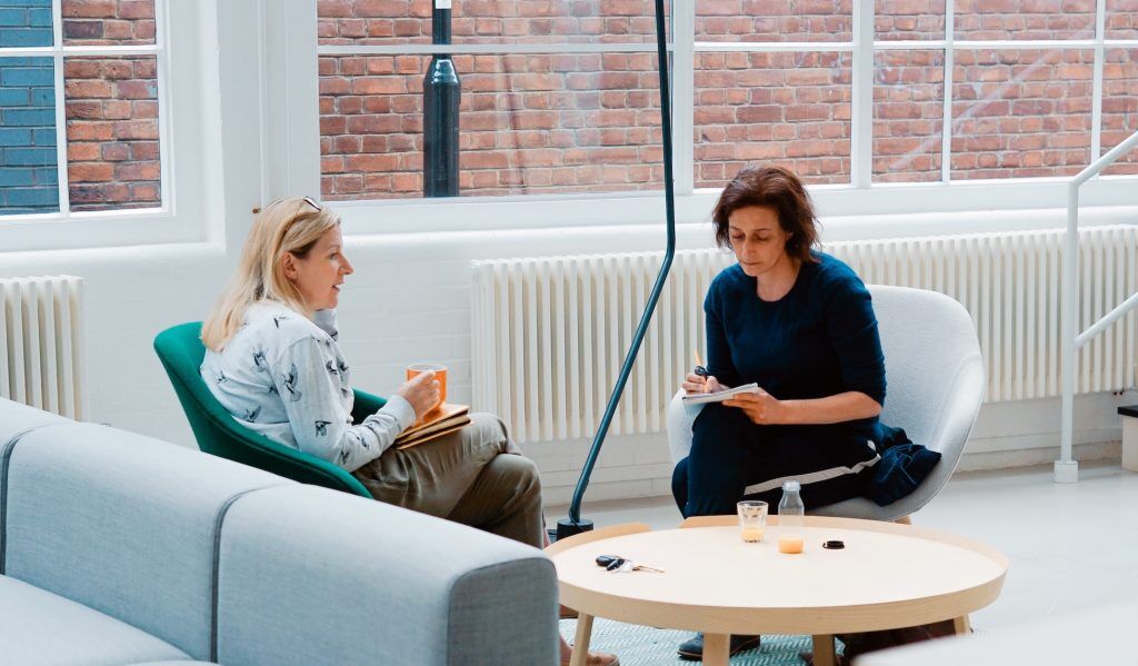 two women chatting over coffee taking notes
